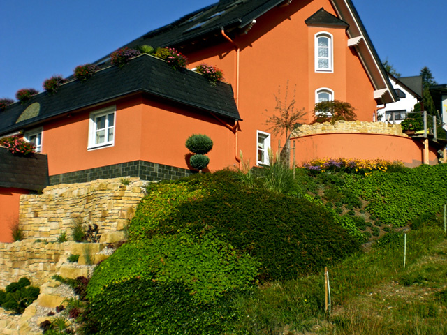 Referenzbild: 13 Sandsteinmauern, bodendeckende Bepflanzung zur Hangsicherung, akzentuiert durch Blütenstauden mit großer Fernwirkung