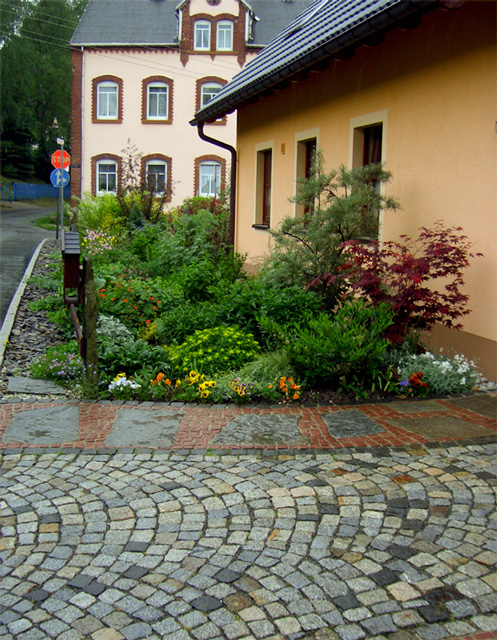 Referenzbild: 27 Zufahrt aus Natursteinpflaster in Kombination mit einem polygonalen Plattenbelag mit Mosaikbänder.